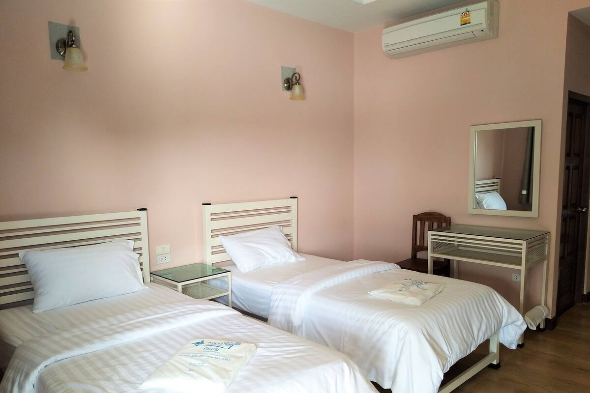 A hotel room with two beds, a bedside table, a mirror, and an air conditioning unit.