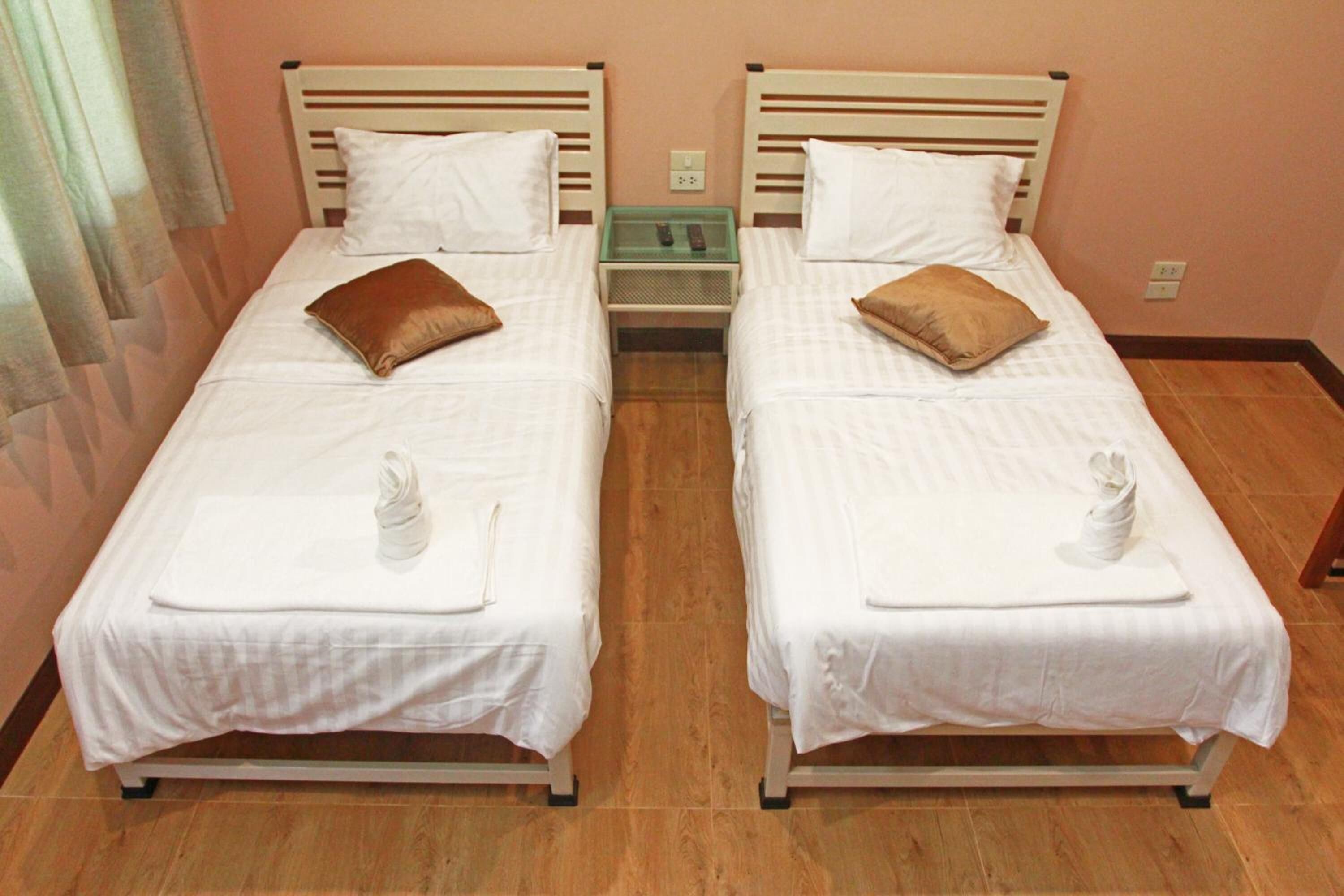 Two single beds with white bedding and brown pillows, a small bedside table with a glass top, and a wooden floor.