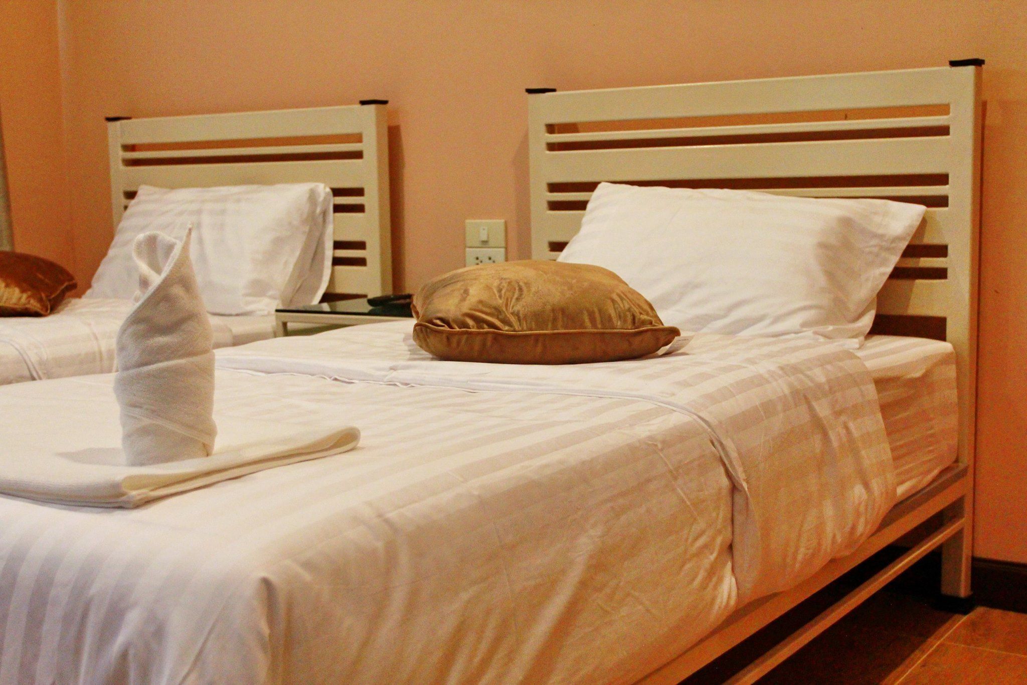 Dos camas individuales con cabeceros blancos y almohadas beige, una bata blanca sobre la primera cama, y una mesita con un teléfono y una lámpara entre las camas.