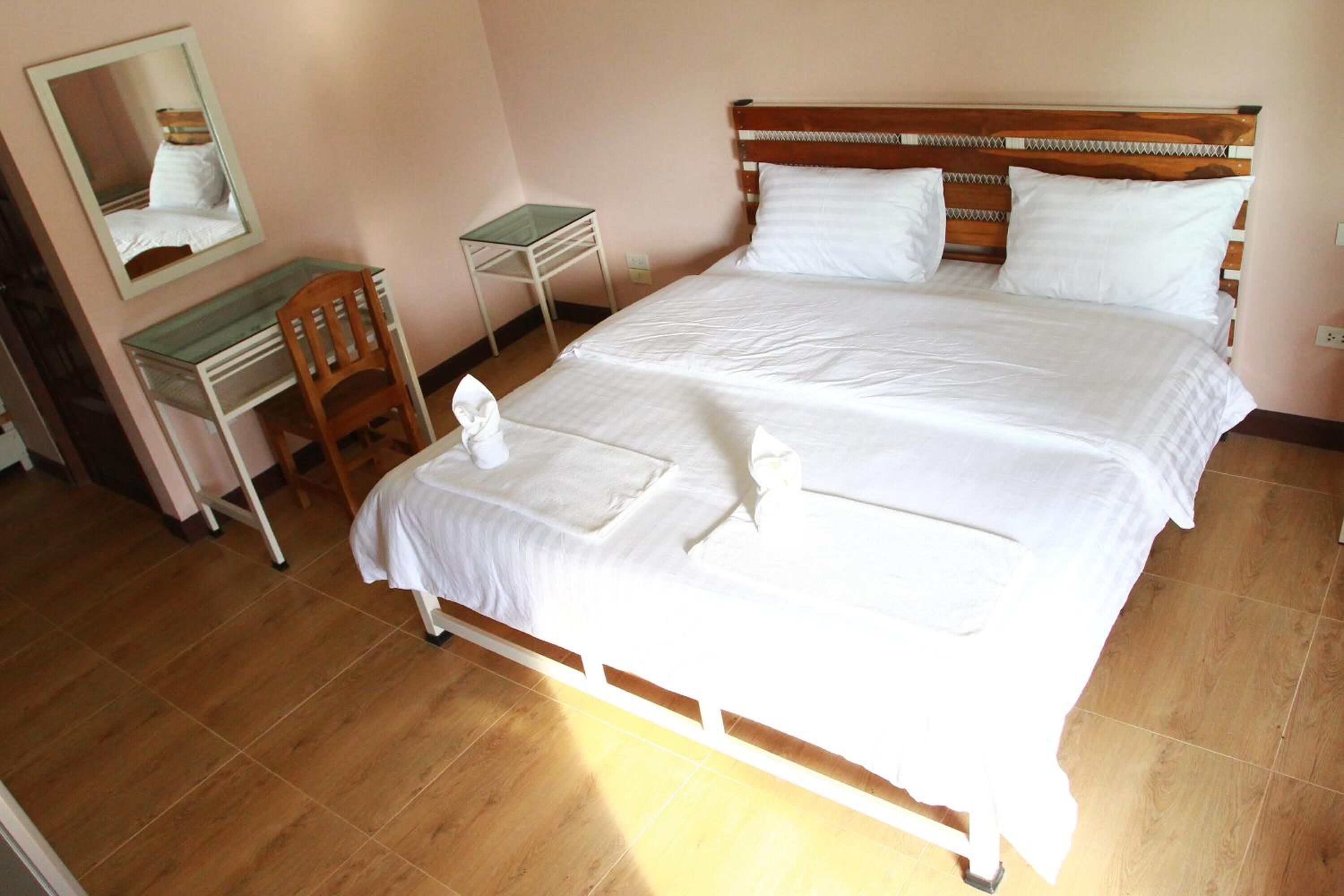 A neatly made bed with white linens, a wooden headboard, and a small desk with a chair.