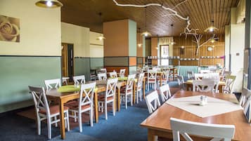 Un espace repas comprenant plusieurs tables et chaises, un plafond en bois et des luminaires suspendus.