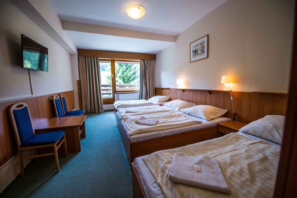 Een hotelkamer met drie bedden, een televisie, een bureau en een stoel.