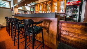 Zona de bar con mostrador de madera, taburetes y un refrigerador de Coca-Cola.