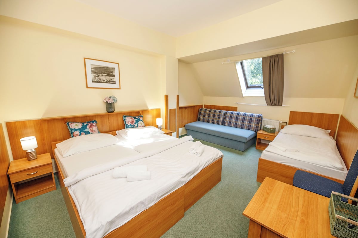 Een hotelkamer met twee bedden, een bank, een tafeltje en een raam met gordijnen.