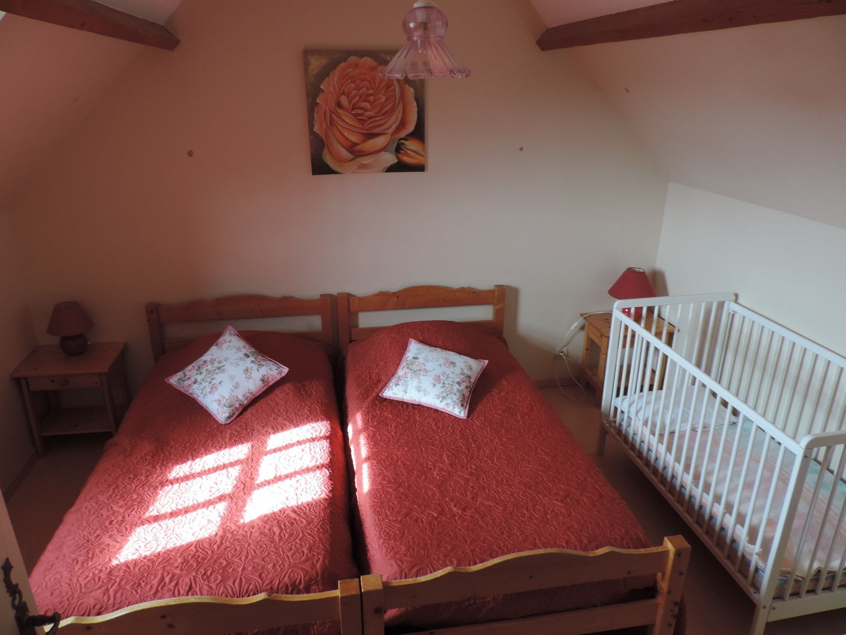 Ein Schlafzimmer mit zwei Einzelbetten, einem Holz-Kopfteil, einem kleinen Nachttisch mit Lampe, einem Babybett und einem Bild an der Wand.