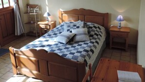 Un dormitori amb un llit de fusta, una taula de nit, una petita estant i una finestra amb cortines.