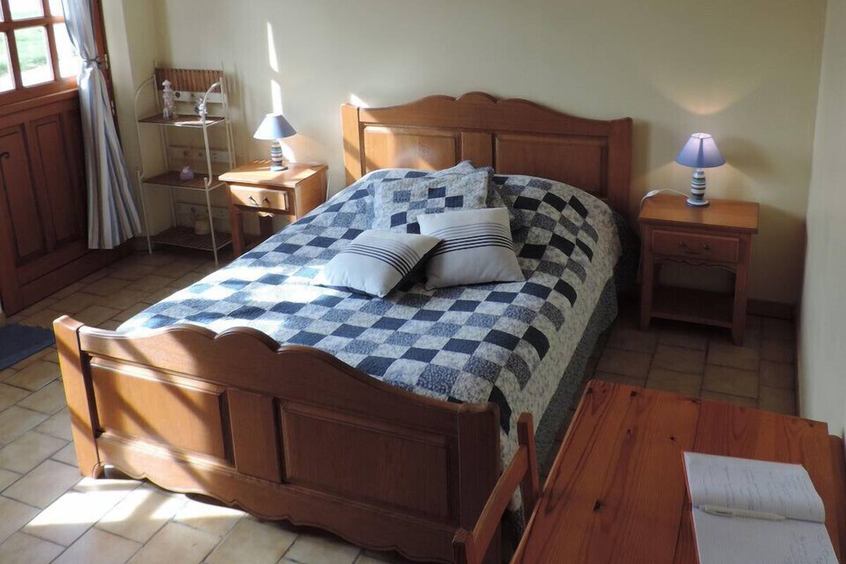 A bedroom with a wooden bed, a bedside table, a nightstand, a window with curtains, and a small shelf.