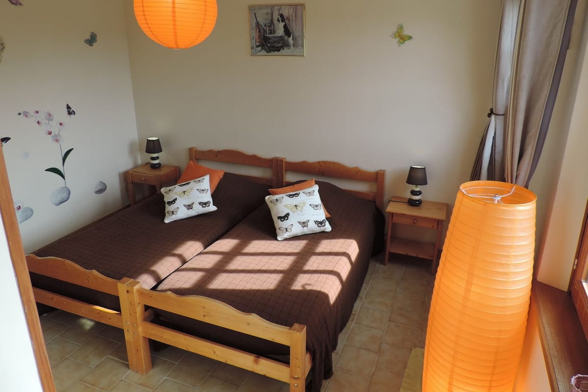 A bedroom with a wooden bed, two nightstands, a wall-mounted lamp, a large orange lantern, and butterfly wall art.
