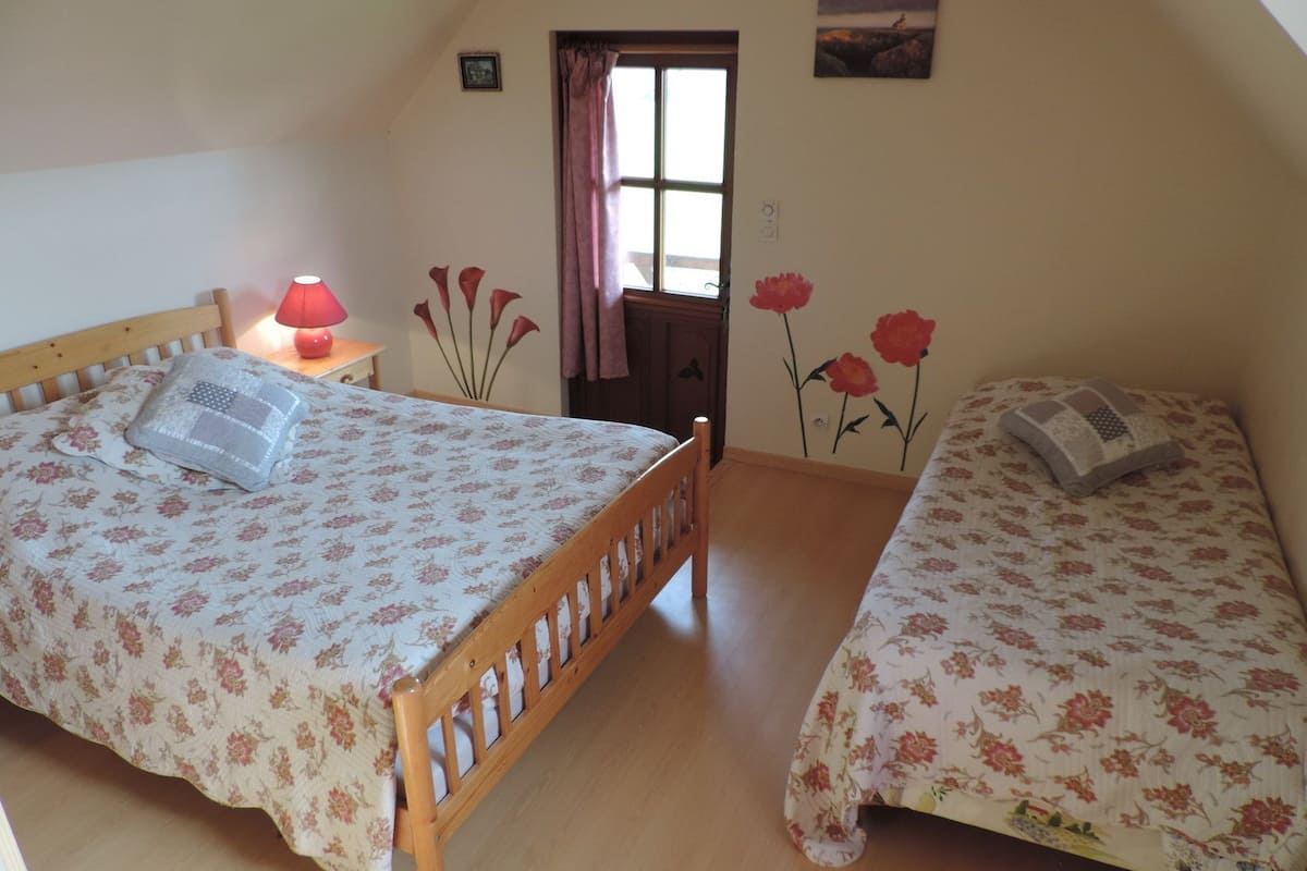 A bedroom with two single beds, a wooden headboard, a nightstand with a lamp, and a door leading outside.
