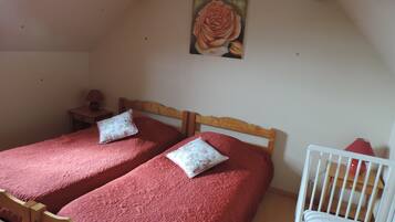 A bedroom with two beds, a crib, a painting, and a lamp.
