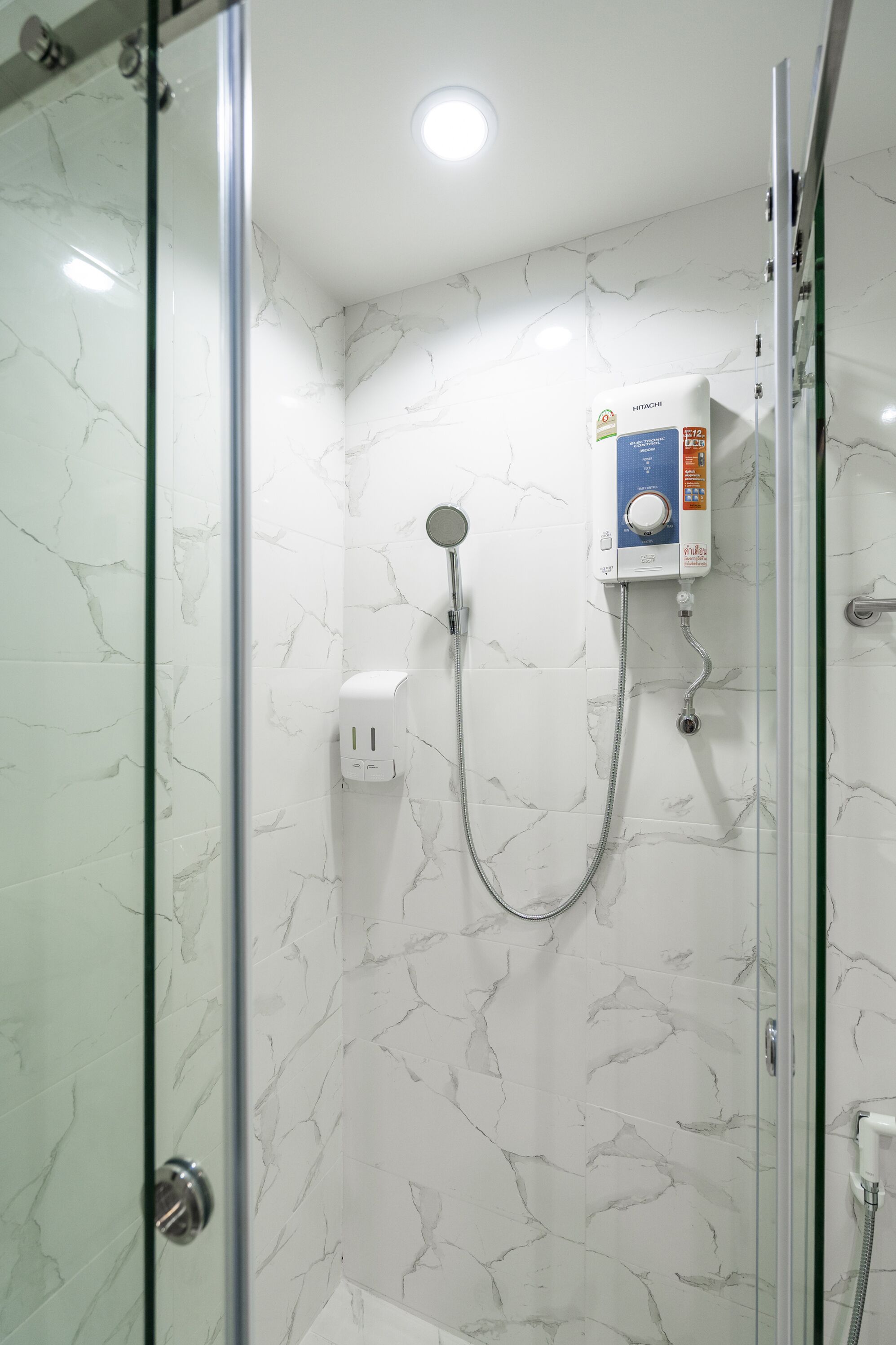 A glass-enclosed shower with a handheld showerhead, a control panel, and a wall-mounted faucet.