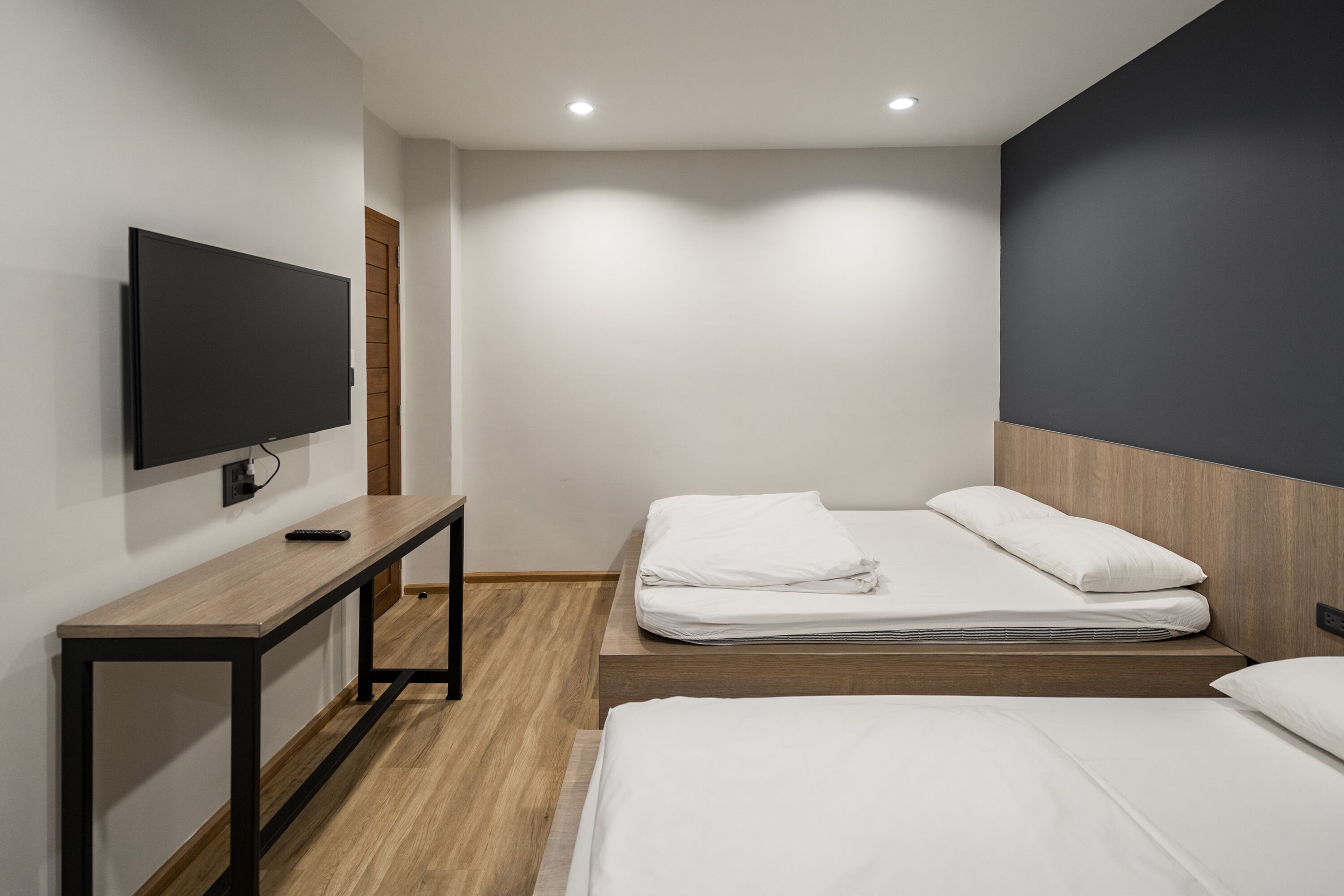 Een moderne hotelkamer met een flatscreen televisie aan de muur, een houten bureau en een bed met witte beddengoed.