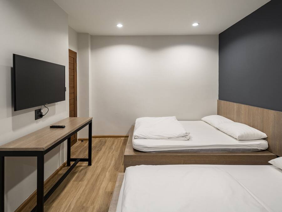 Een moderne hotelkamer met een flatscreen televisie aan de muur, een houten bureau en een bed met witte beddengoed.