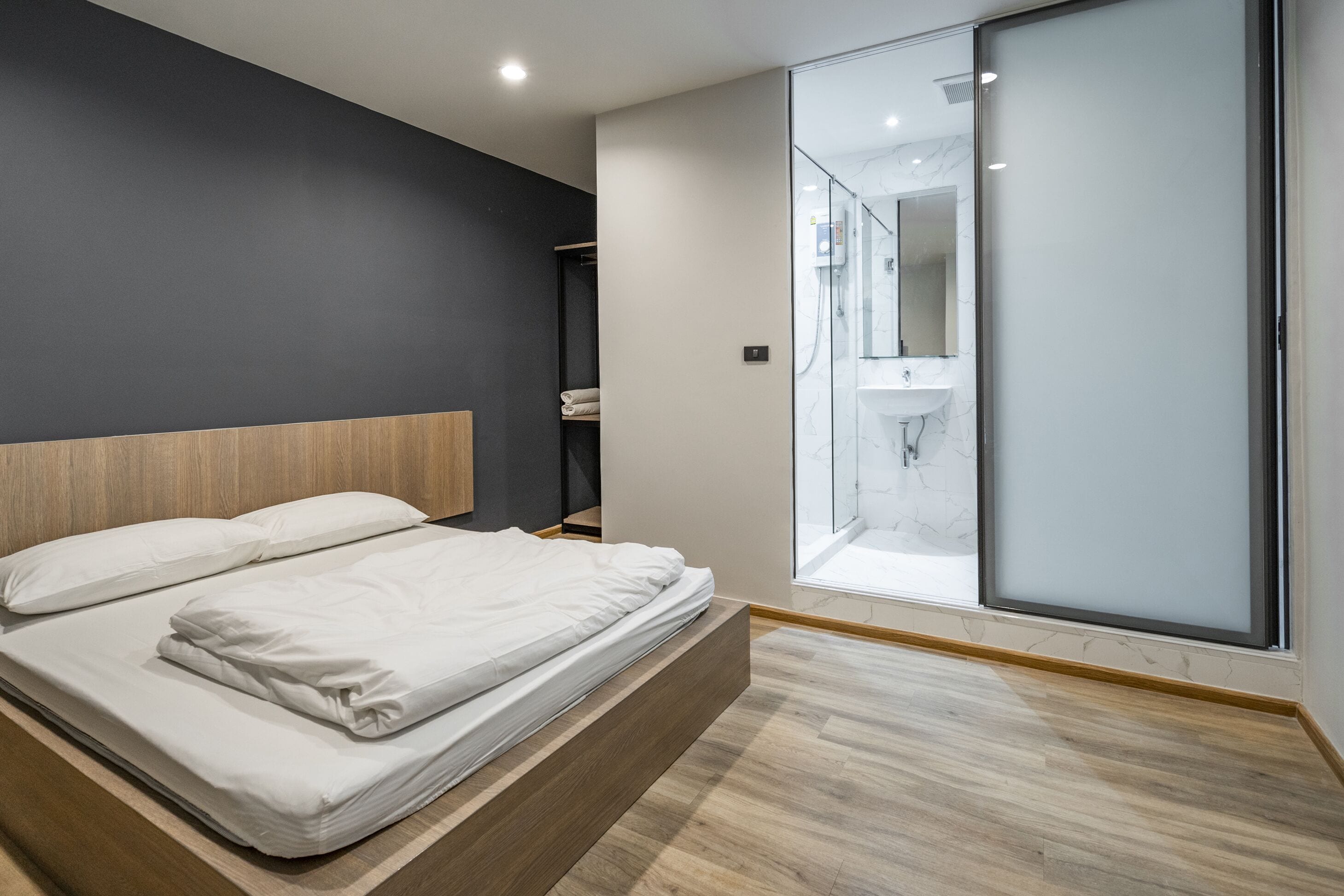 Quarto moderno com cabeceira de madeira, uma cama grande, porta de vidro que dá para um banheiro e piso de mármore.