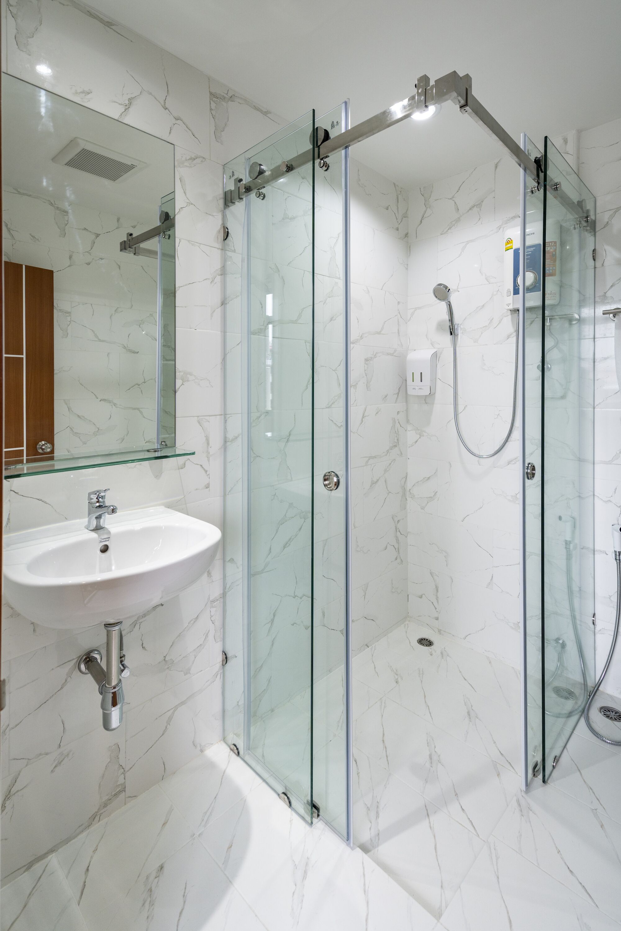Un baño moderno con ducha envuelta en vidrio, un lavamanos blanco y paredes con diseño de mármol.
