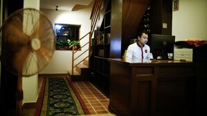 Un hombre sentado en un escritorio de madera, con una computadora, una estantería y una escalera al fondo.