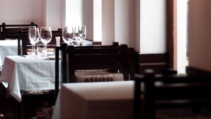 Un restaurante con mesas dispuestas para comer, candelabros colgantes y amplias ventanas.