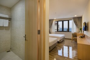 Habitación de hotel con ducha, cama, escritorio y vista al mar.