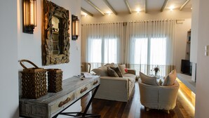 Una sala de estar moderna con una mesa de centro de madera, un sofá blanco y un sillón con cojines. Hay un espejo grande con marco rústico e iluminación instalada en la pared.