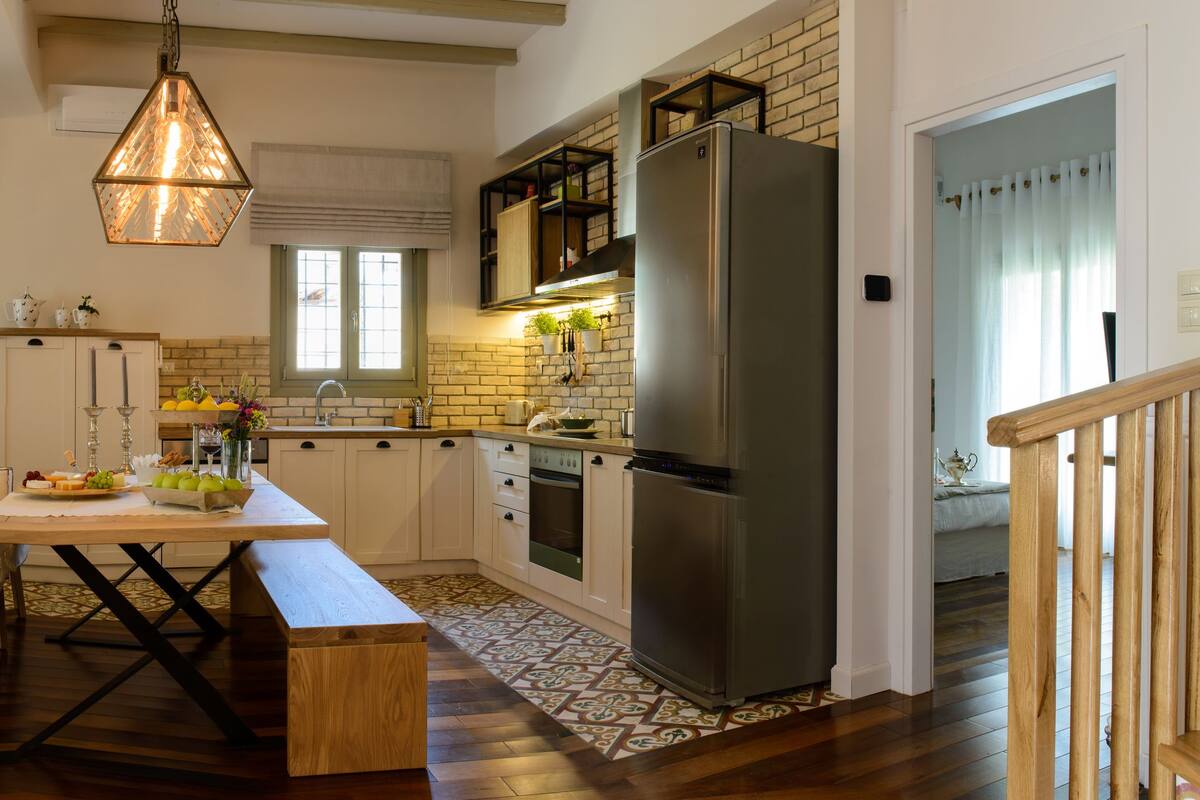 Una cocina moderna con un refrigerador grande, piso de madera y un comedor con banco y sillas.