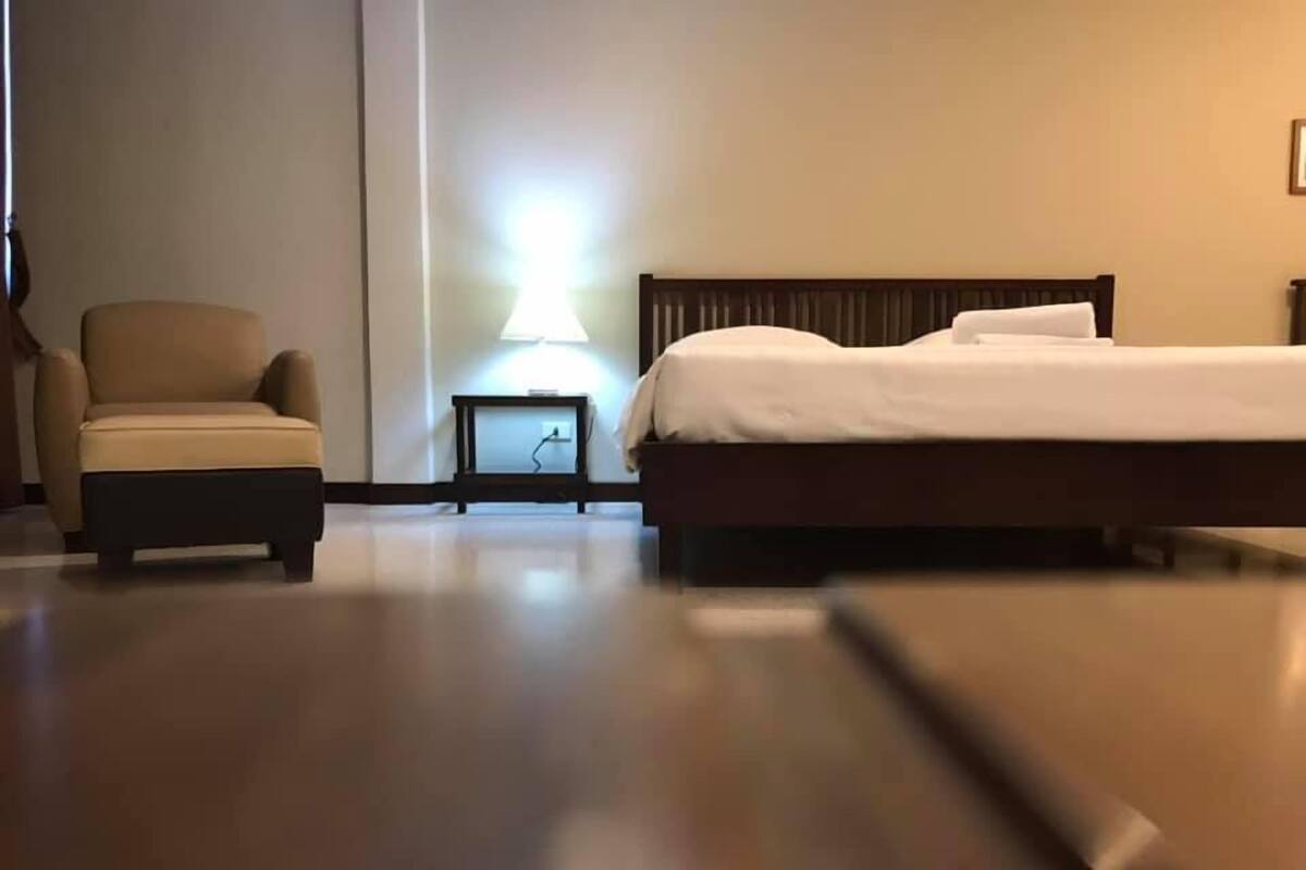Una habitación de hotel con una cama, una silla, una mesita de noche y una lámpara.