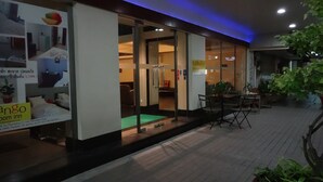 L'ingresso di un hotel con porte in vetro, un cartello con la scritta 'Mango Room Inn' e una zona esterna con tavoli e sedie.