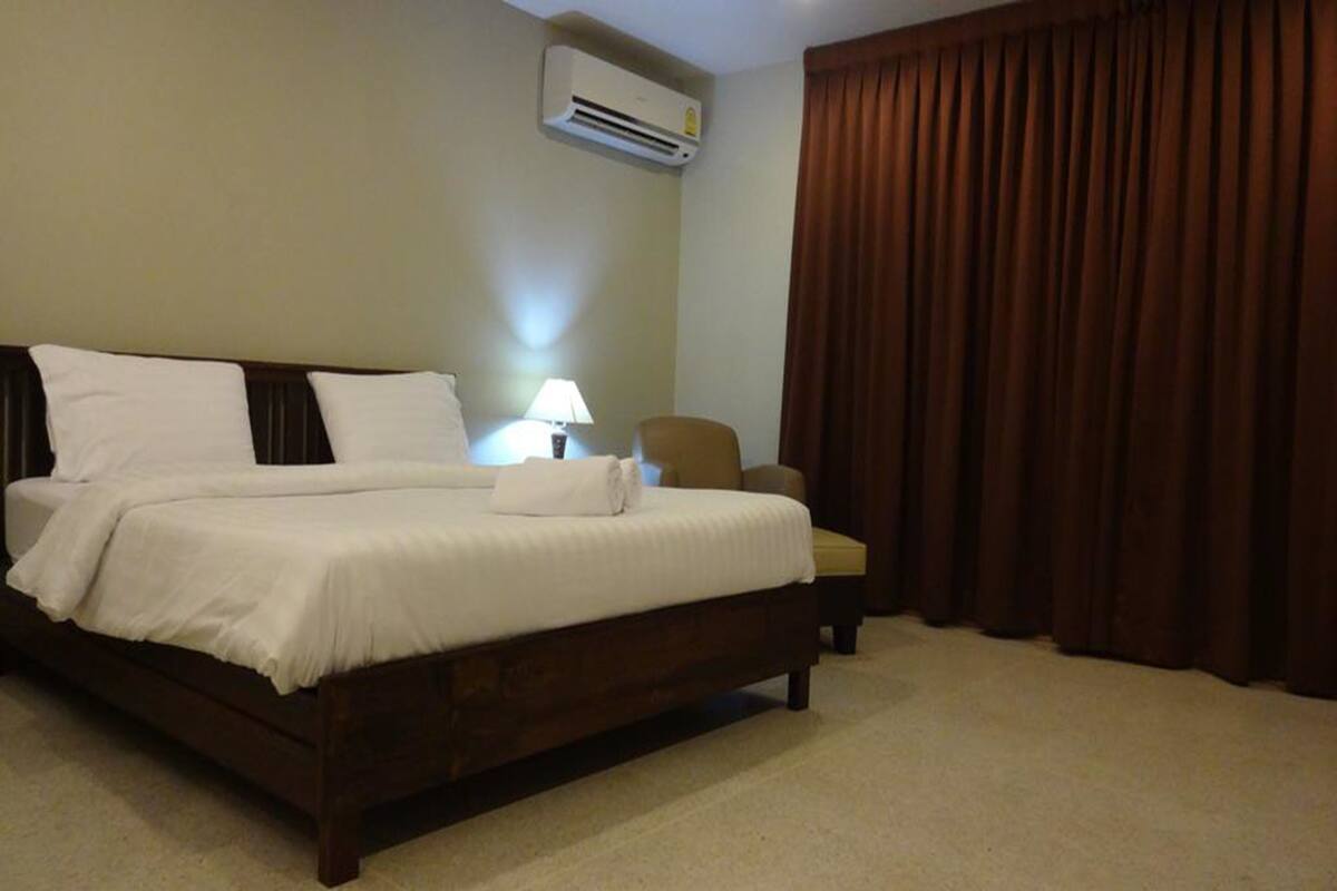 Una habitación de hotel con una cama grande, una silla, una lámpara y un ventanal con cortinas.
