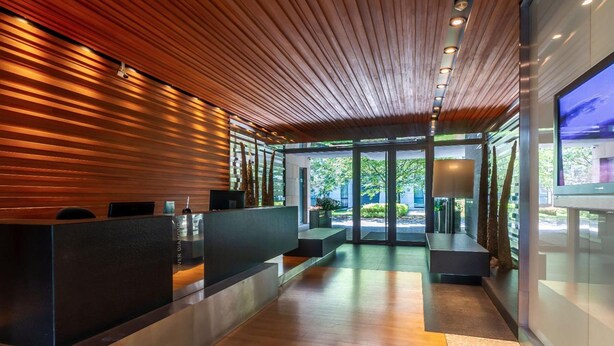 A modern reception area with wooden slats on the ceiling, a reception desk, and a large window offering a view of the outdoors. - Luxury apartment River Diamond residence (Prague)