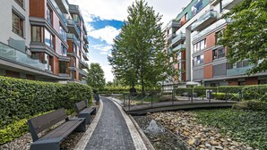 A pathway flanked by benches and a water feature, leading to a modern apartment complex with balconies and a well-maintained garden. - Luxury apartment River Diamond residence (Prague)