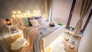 A bedroom with a bed, bedside table, and a window with blinds. - Luxury apartment River Diamond residence (Prague)