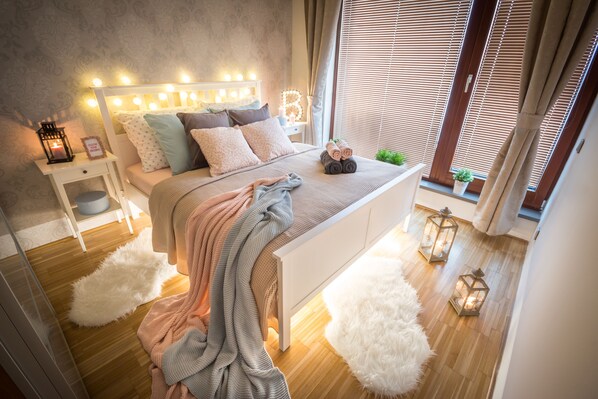 Quarto com cama, mesa de cabeceira e janela com persianas.