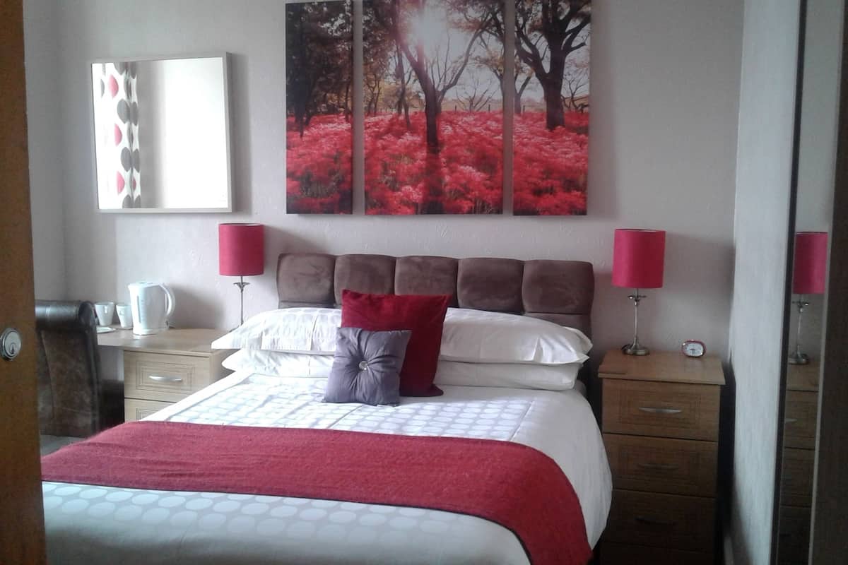 Ein Schlafzimmer mit einem Bett, zwei Nachttischen, einem Schminktisch, einem Spiegel und einem Bild an der Wand.