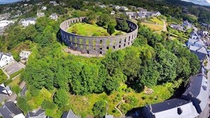 A circular stone structure surrounded by lush greenery and residential buildings. - Adelphi Villa (Oban)