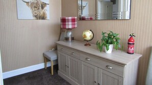 A room with a light-colored wooden cabinet, a small desk, a red and white checkered lamp, a globe, a potted plant, and a fire extinguisher. - Adelphi Villa (Oban)