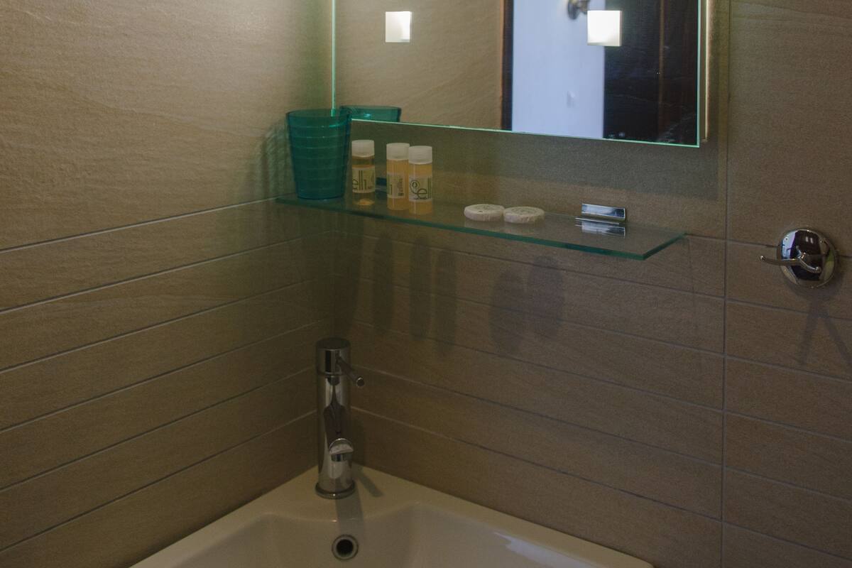 Un baño con un lavabo blanco, un espejo con iluminación y un estante de vidrio con artículos de aseo.