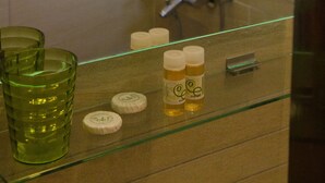 A bathroom with a glass shelf holding toiletries and a green glass. - Elli Hotel (Skopelos)