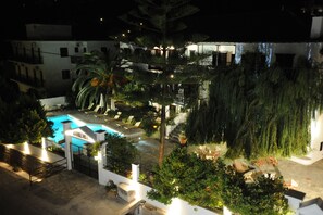 A nighttime view of a hotel courtyard with a swimming pool, palm trees, and outdoor seating areas. - Elli Hotel (Skopelos)