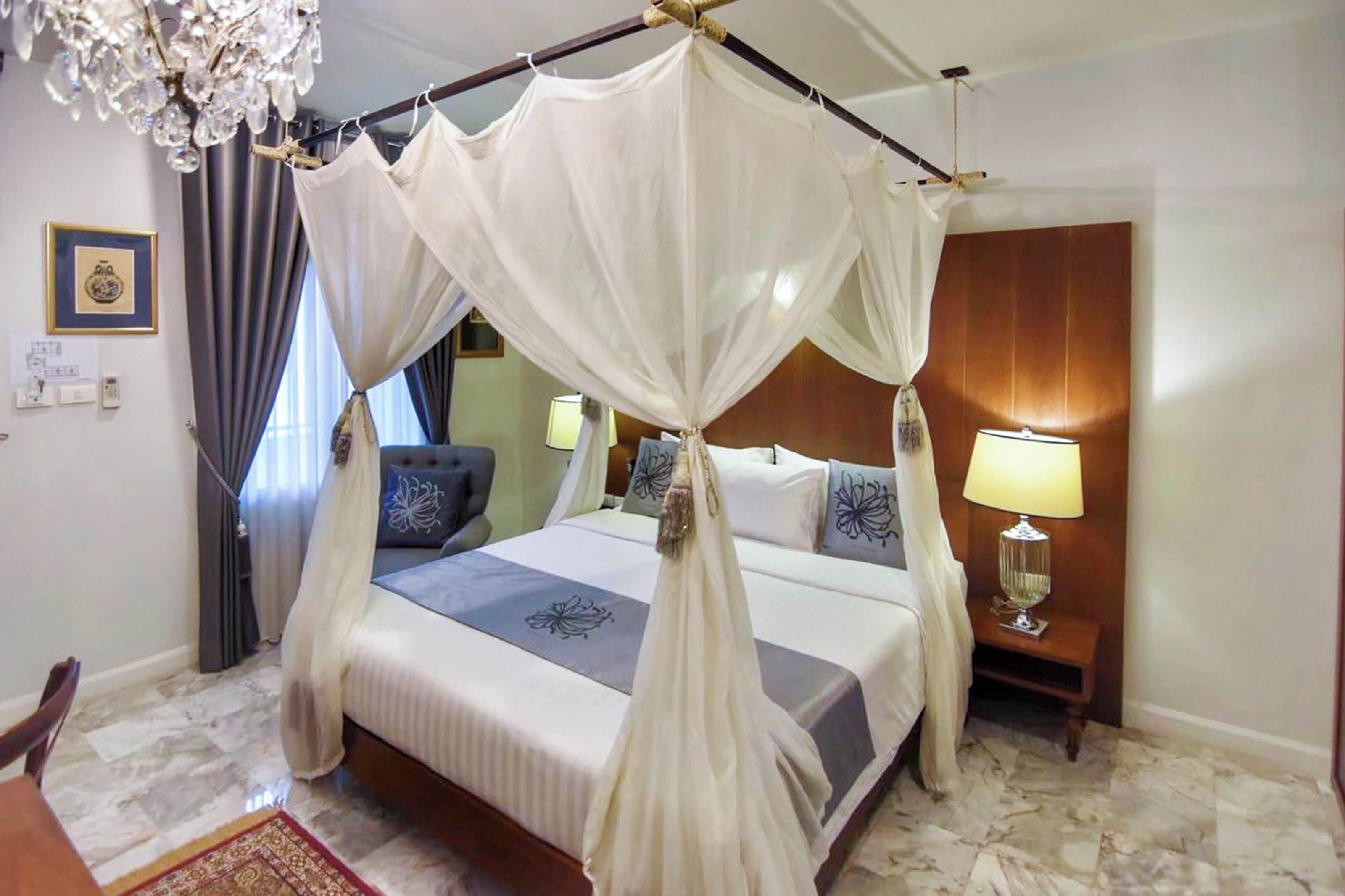 A four-poster bed with a canopy, a wooden headboard, two bedside lamps, and a marble floor.