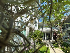 A courtyard with a white building, a covered seating area, and various plants. - Villa Amphawa (Amphawa)