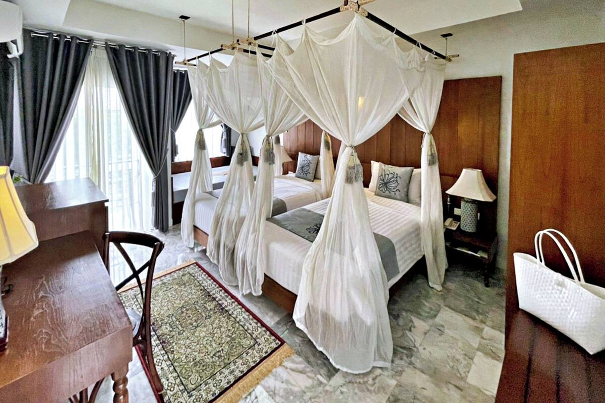 A bedroom with a four-poster bed, a desk, a chair, a lamp, and a bedside table.