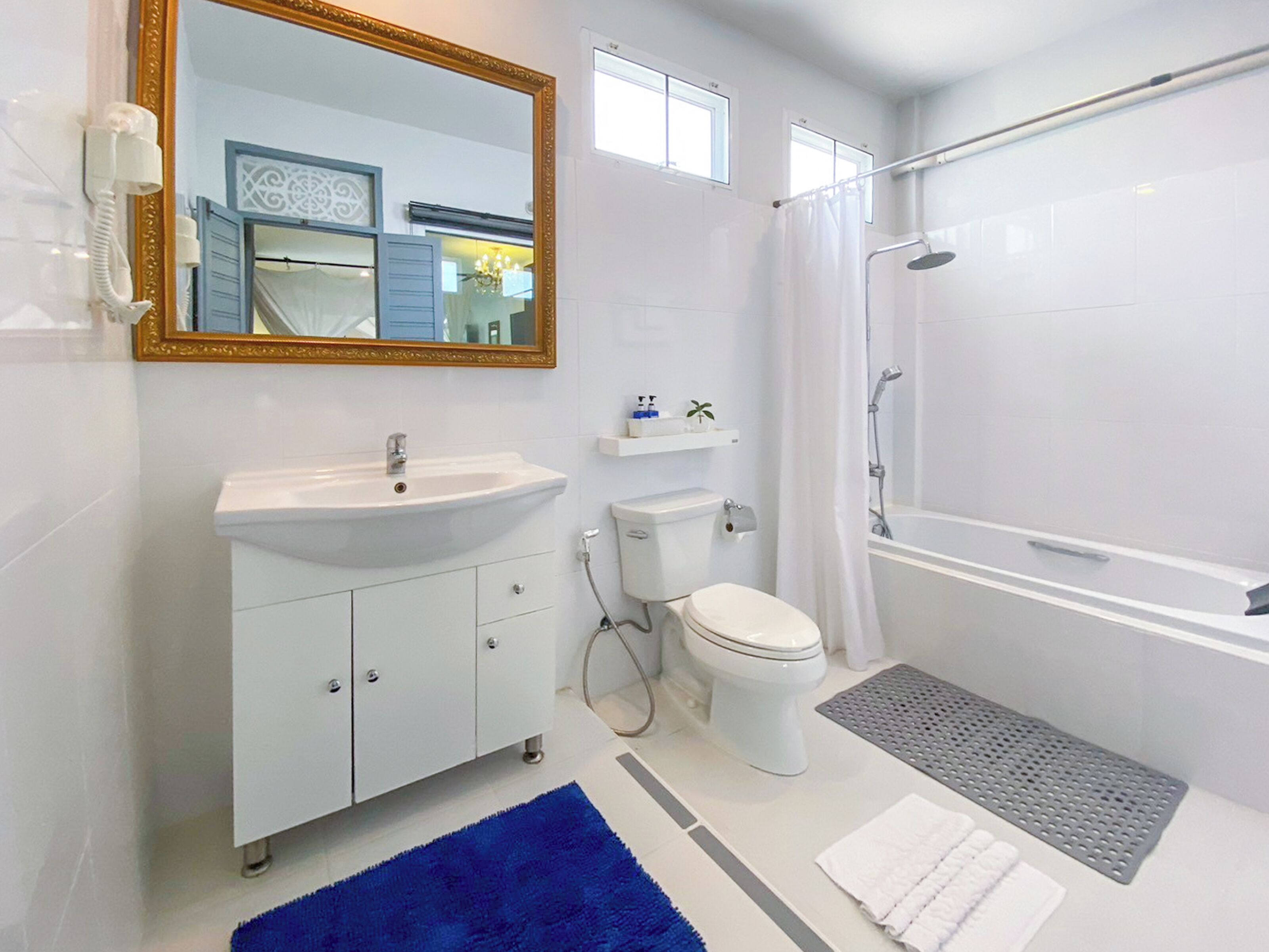 A modern bathroom with a white sink, toilet, and shower. There is a blue rug on the floor and a white towel on the counter.