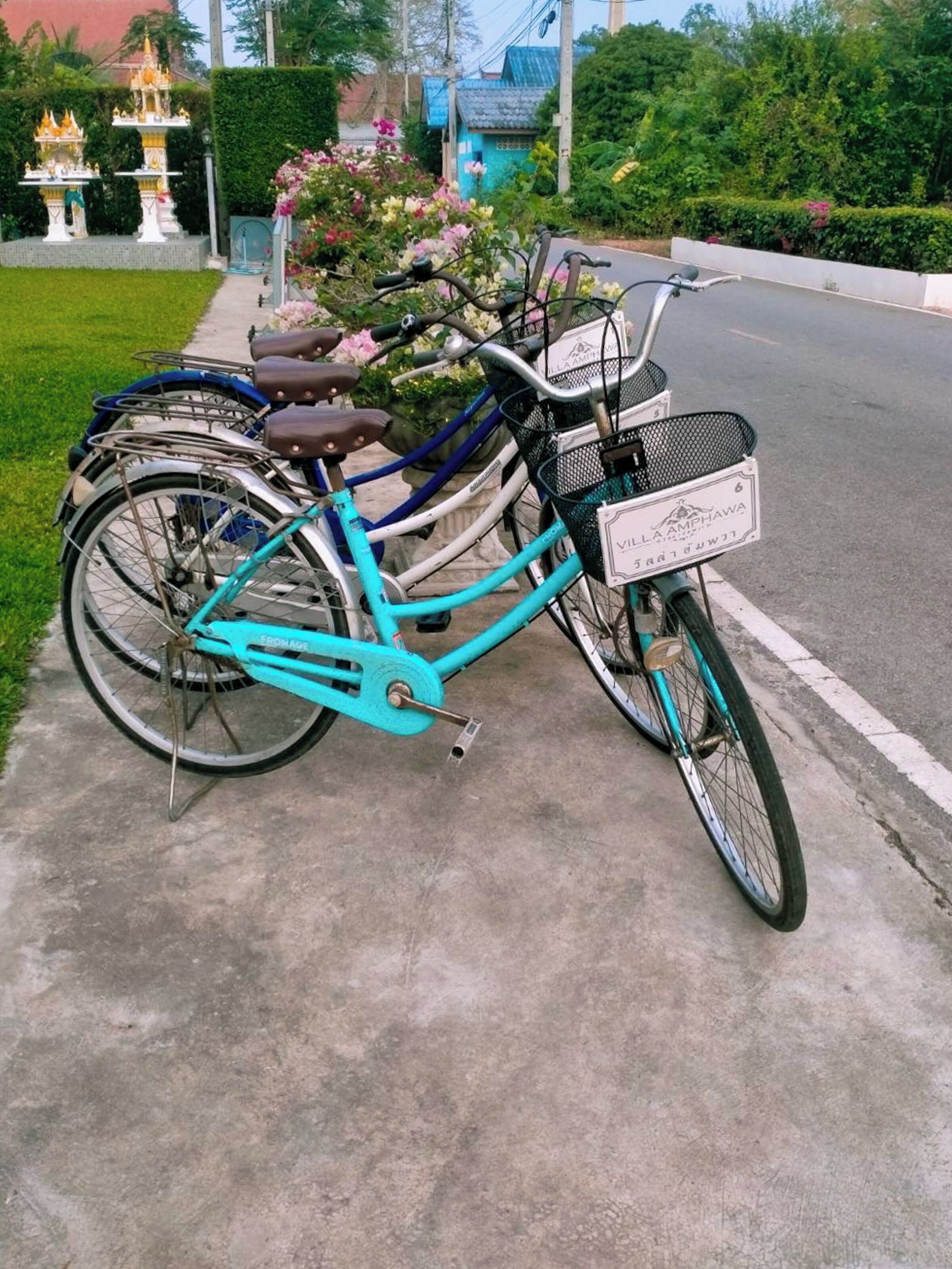 A turquoise bicycle parked on a sidewalk with a basket and a sign that reads "Villa Ampawa."