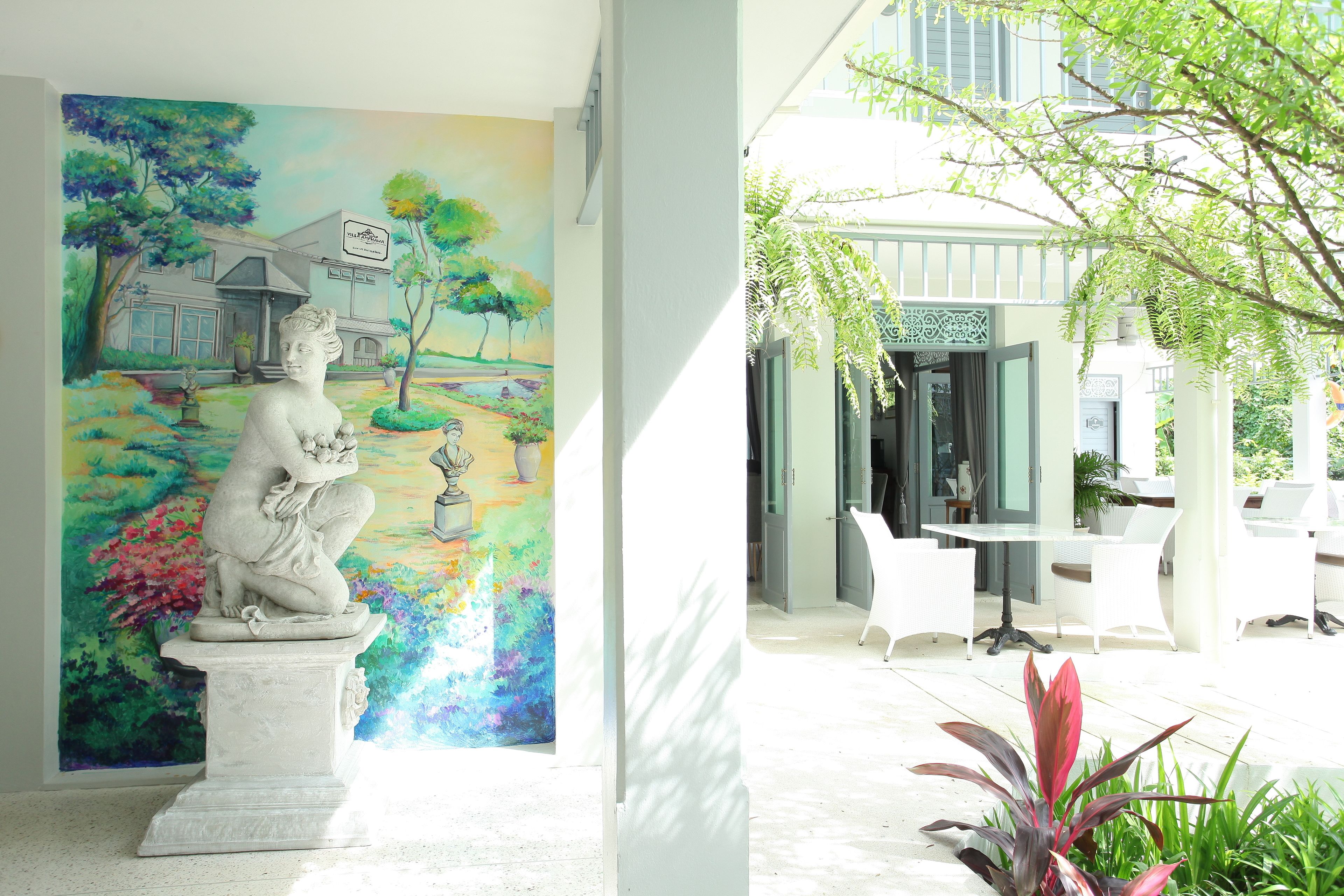Une statue dans une cour, avec une fresque colorée en arrière-plan et un espace de détente extérieur moderne.