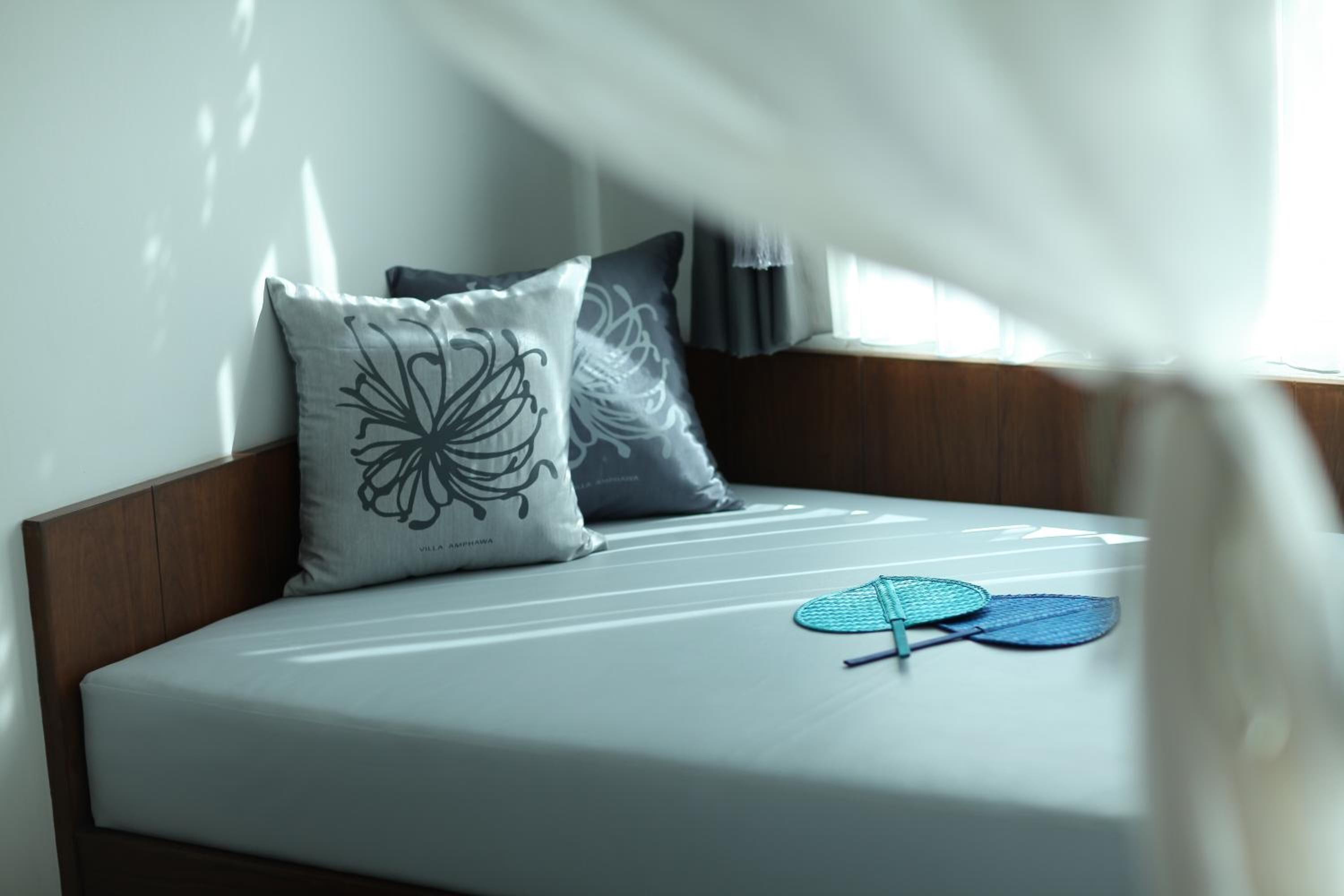 Un letto ben rifatto con un materasso bianco, due cuscini con un motivo floreale e una ventola blu sopra il letto.