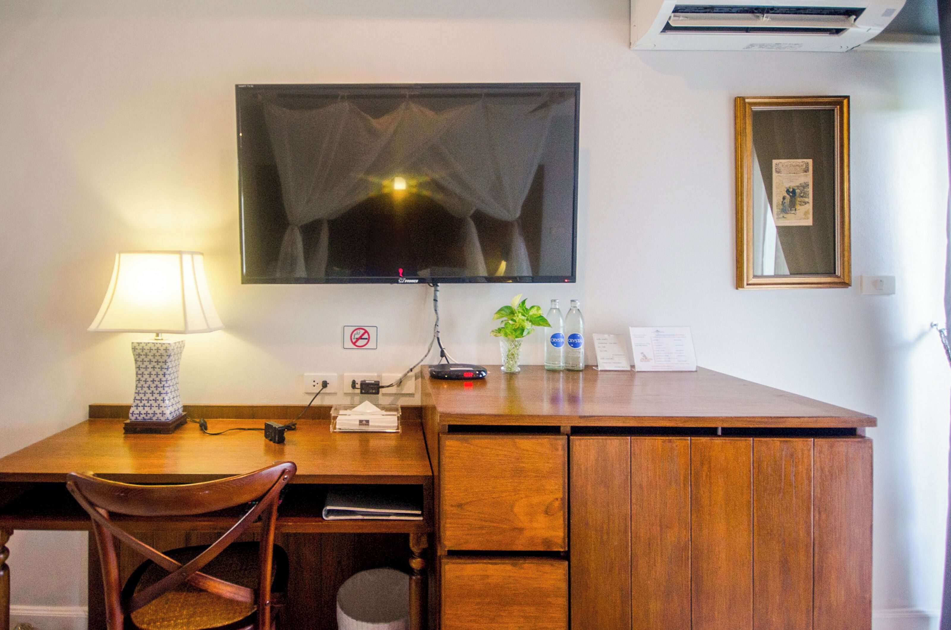 A wooden desk with a lamp, a television, a plant, and a framed picture on the wall.