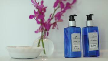Two blue bottles labeled 'Body Lotion' and 'Soap' next to a white bowl and a vase with pink flowers.