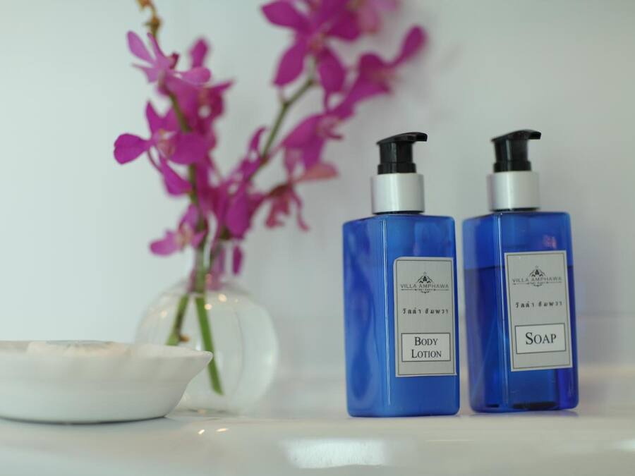Two blue bottles labeled 'Body Lotion' and 'Soap' next to a white bowl and a vase with pink flowers.