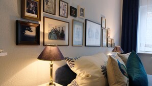 A room with a bed, a nightstand, a lamp, and a wall decorated with framed pictures. - Residenz am Berg (Leimen)