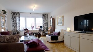 A living room with a sofa, a TV, and a dining area with a table and chairs. - Residenz am Berg (Leimen)