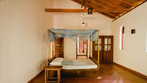 A room with a bed, a wooden bench, a ceiling fan, and a window.